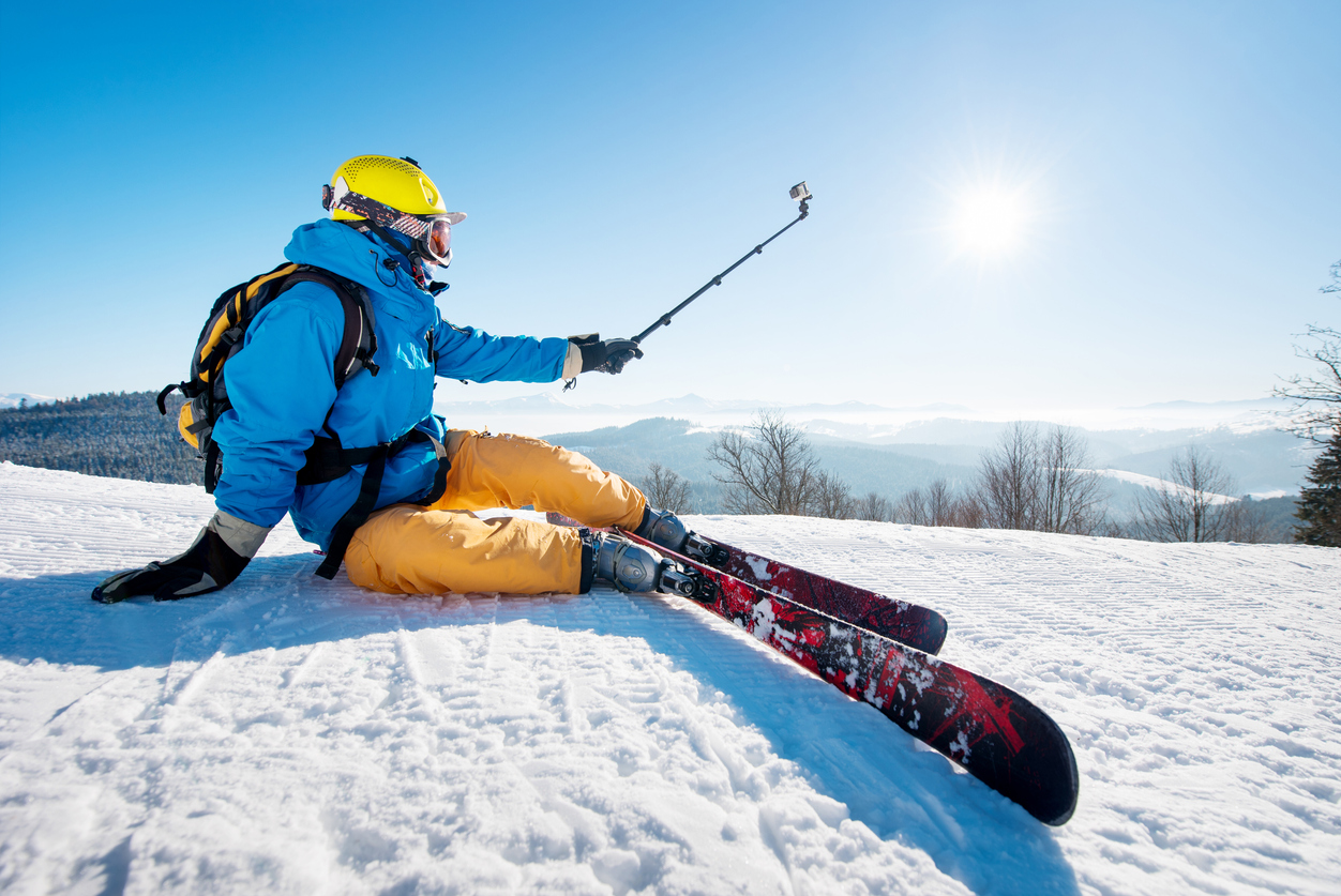 Shot of a skier sitting on the ski slope taking a selfie using selfie stick resting relaxing extreme recreation active lifestyle activity technology smart phone mobility internet online concept.